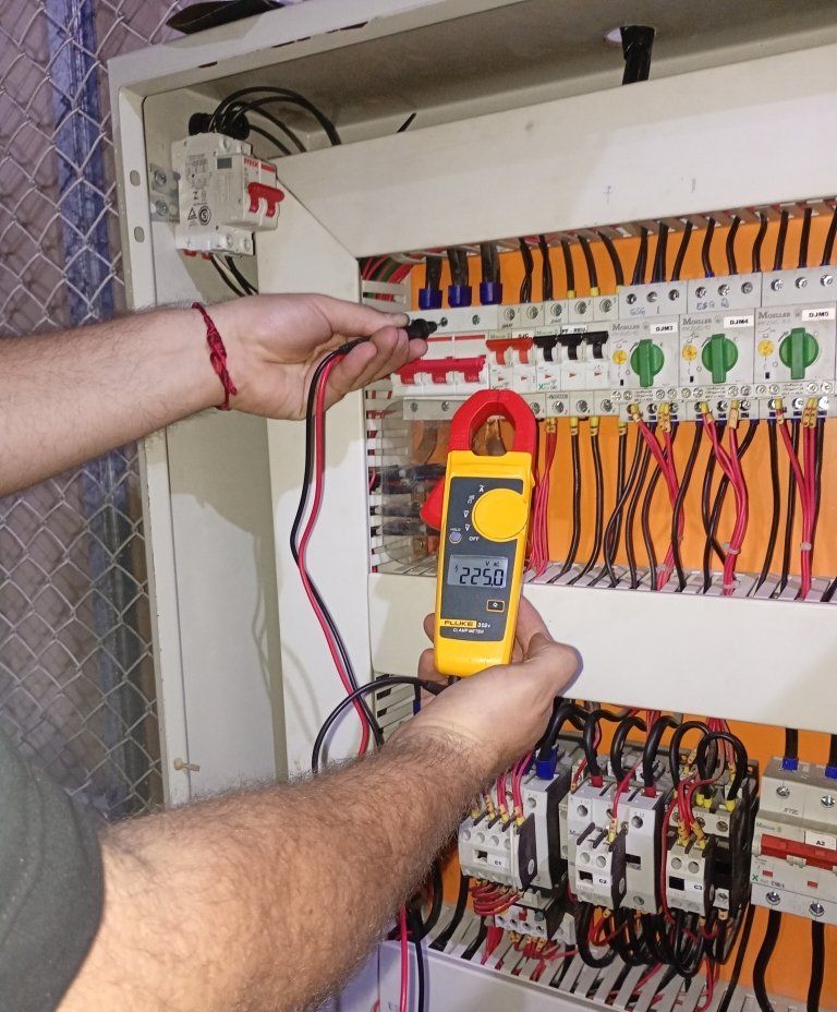 Técnico medindo corrente com alicate amperímetro em quadro de comando
